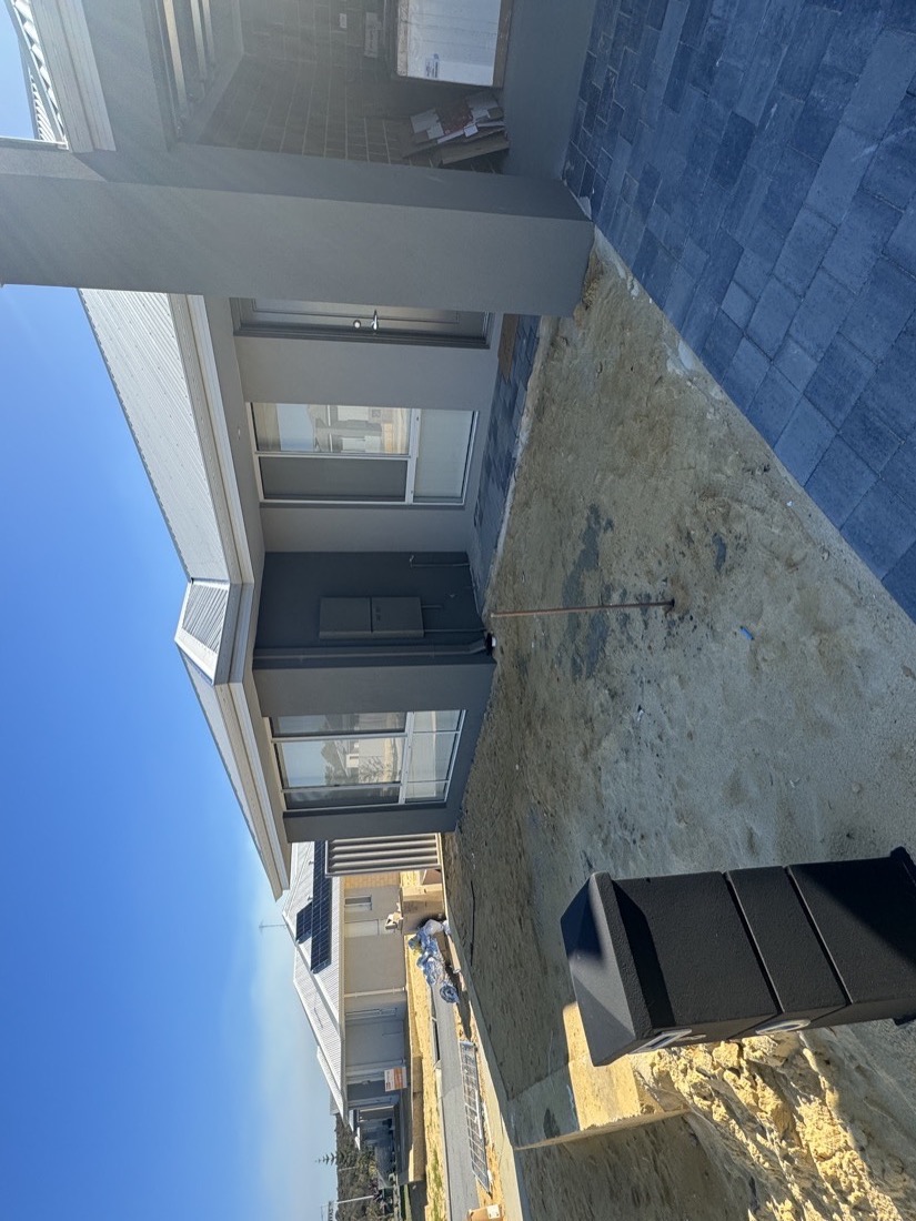Bare sand front yard at a new build, with brick paving and a wheelie bin out front, before installation.